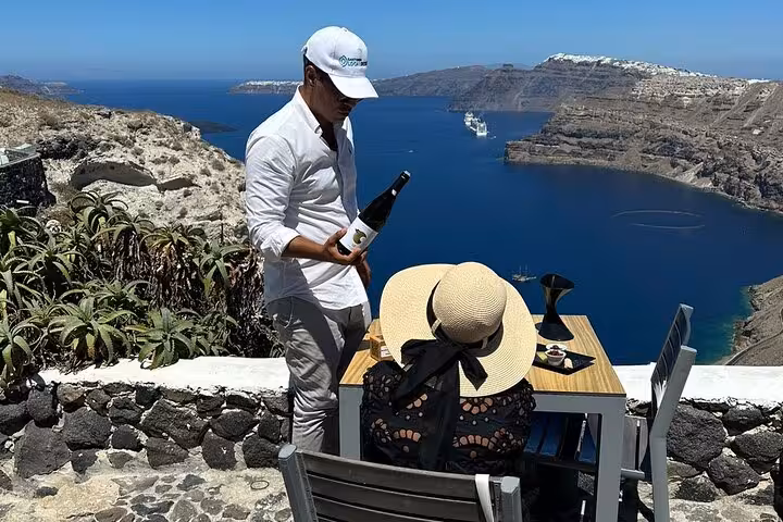 Sommelier pouring Santorini wine at caldera viewpoint, private wine tour visiting top 3 wineries