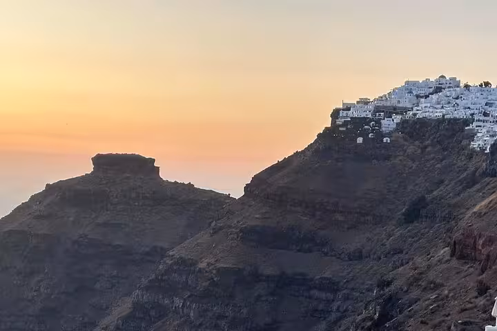 Sunset view of whitewashed Santorini village on caldera cliffs, a highlight of the Island of Thera one-day tour