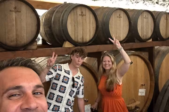 Guests pose in a Santorini winery barrel room during sunset wine tour with tapas and two winery visits