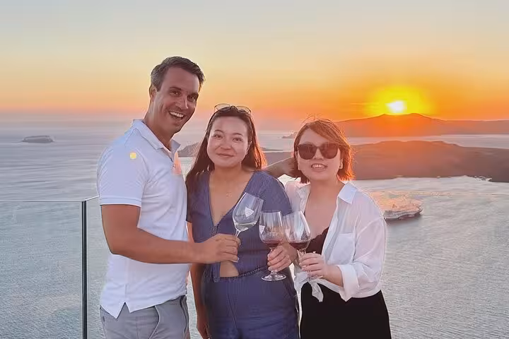 Friends toast wine at Santorini sunset overlooking caldera, on best views tour with 2 wineries and tapas pairing