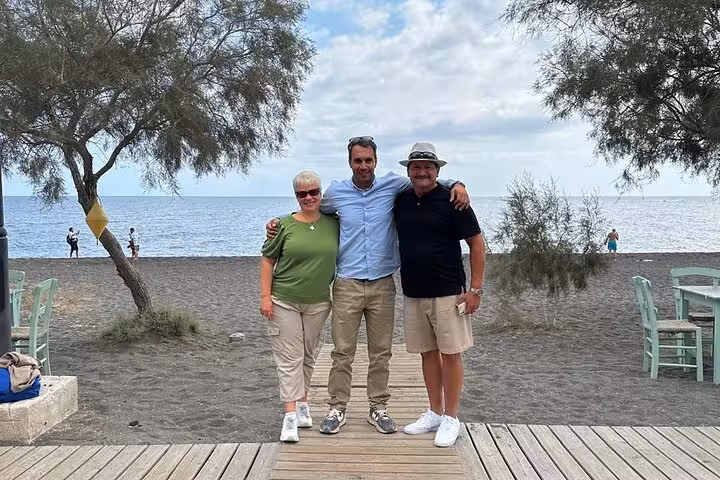 Guests with local guide on Santorini black sand beach during Thera day tour with lunch and winery visit