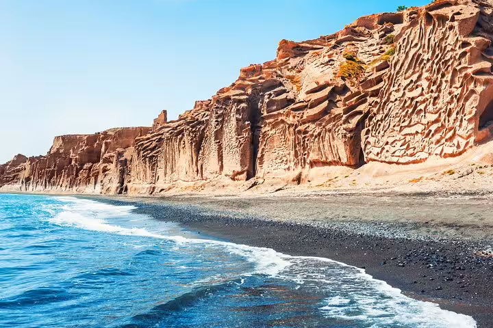 Red volcanic cliffs and black sand shoreline at Vlychada Beach, a stop on a private half-day Santorini tour