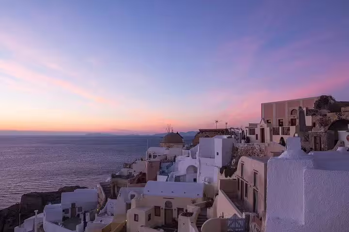 Santorini's iconic whitewashed buildings glow under a vibrant sunset sky, offering a magical view for nighttime sightseeing tours.