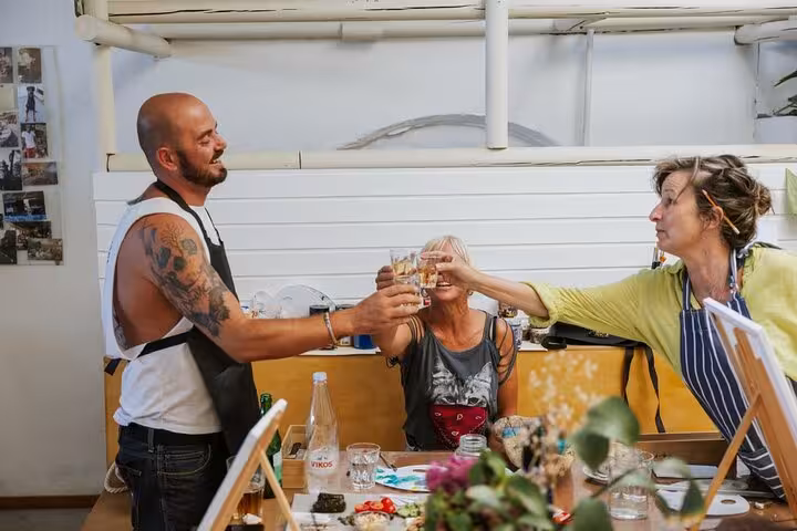 Friends clinking glasses of Santorini wine during a paint class, fun creative workshop with local tastings