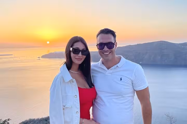 Couple enjoying Santorini caldera sunset during wine and paint tour, scenic photo stop with Aegean views