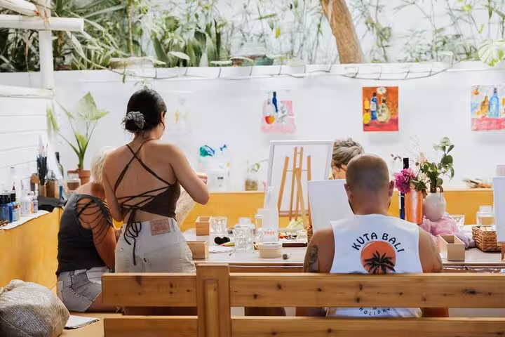 Guests painting at a bright studio during Santorini wine and paint tour, sipping local Greek wine