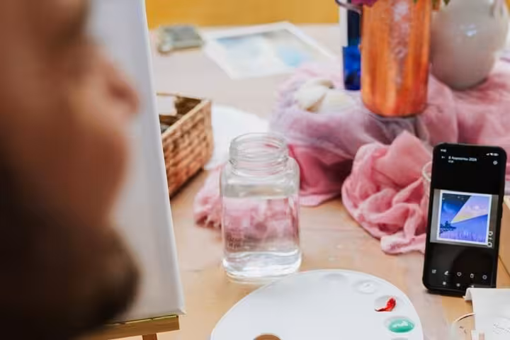 Artist uses phone reference beside palette on Santorini wine and paint adventure, guided paint and sip workshop