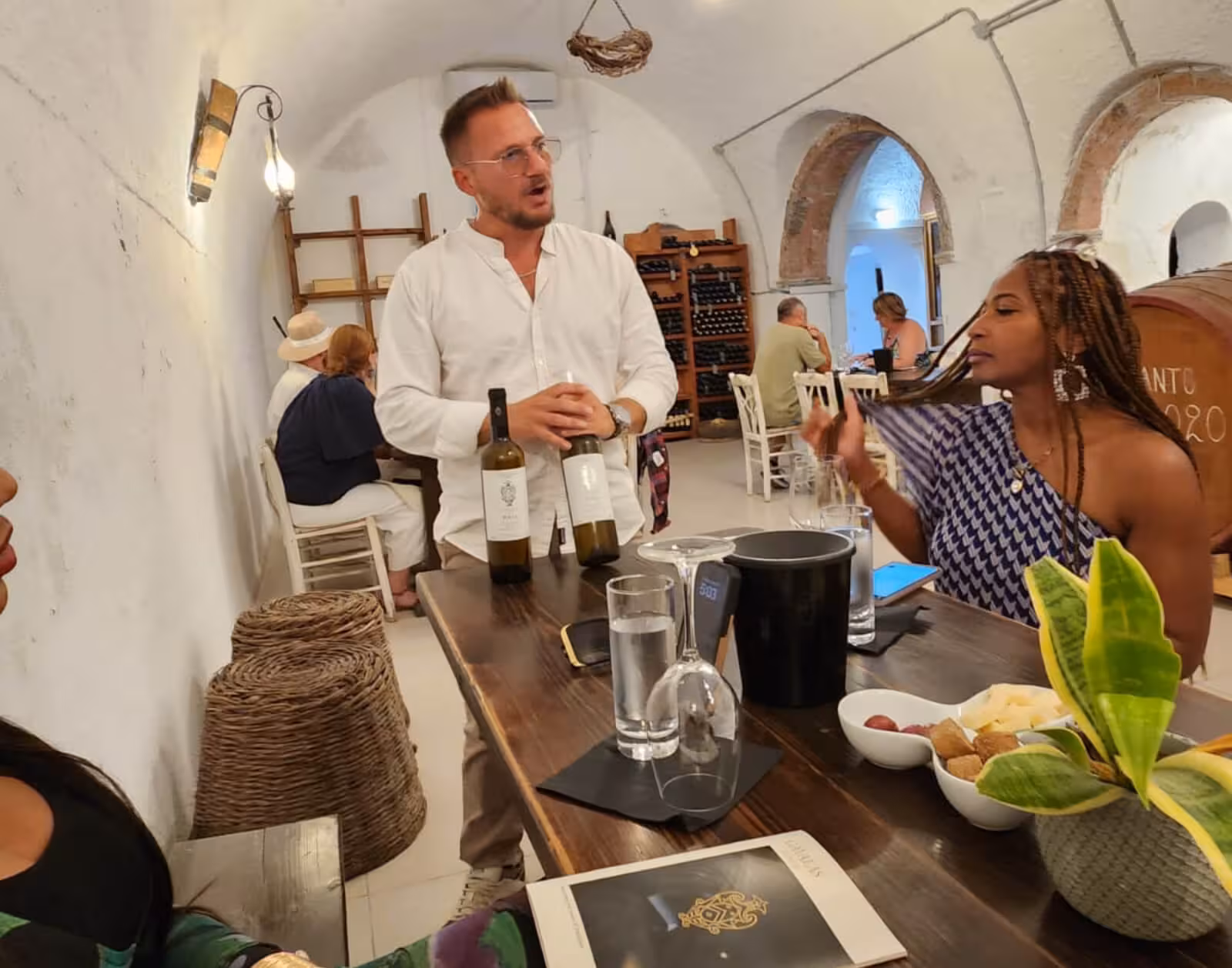 Guide presents Santorini wines in a traditional winery cellar during a private day or sunset wine tasting tour