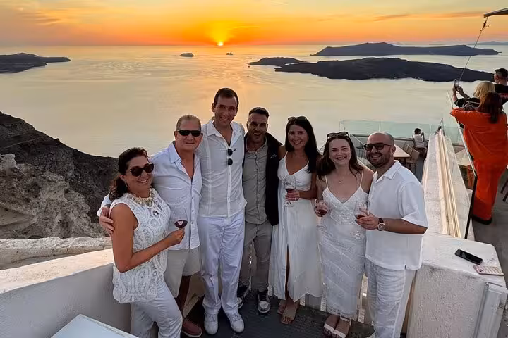 Friends toast local Santorini wine at caldera sunset viewpoint on 2-winery tasting tour with tapas
