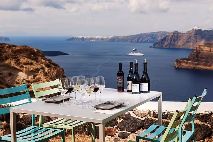 Santorini caldera wine tasting setup with Greek wines and glasses on terrace, Greece Wine Roads tour