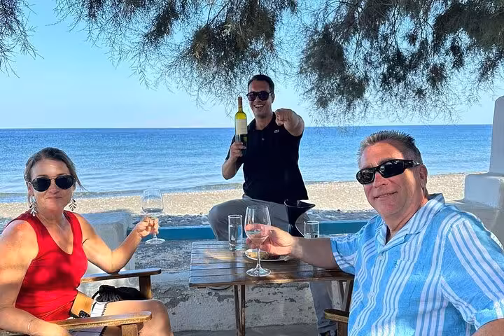 Guests toast Santorini wine by the beach with private guide, part of a top 3 wineries tour with views