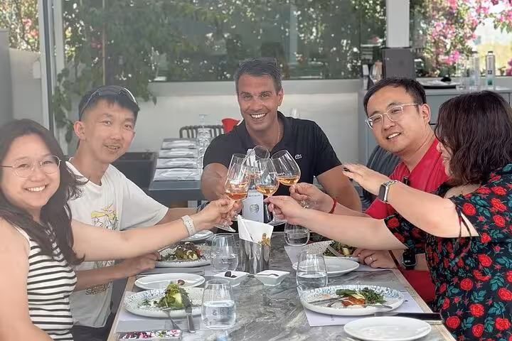 Friends toast Santorini wines during a private winery tour lunch, sampling local varietals with caldera views