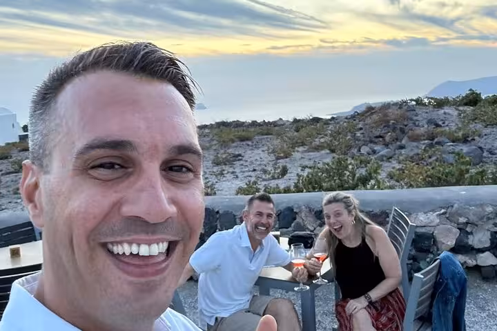Sunset stop on a private Santorini wine tour, friends sip local wine with panoramic island views