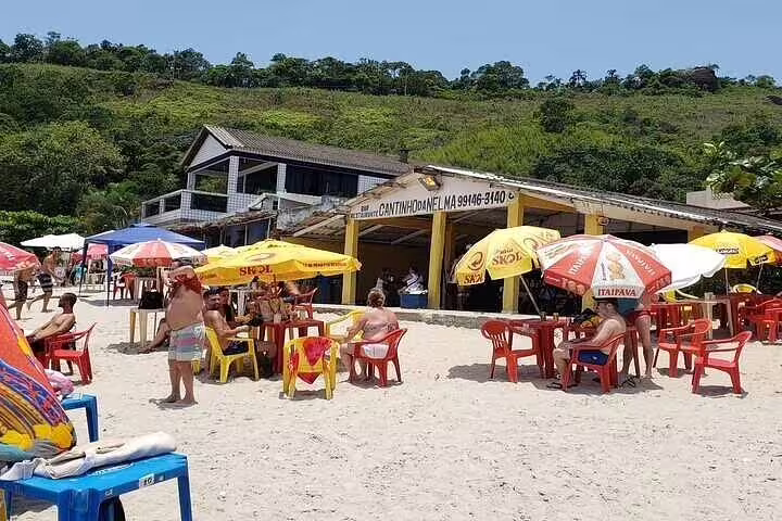 Beachside restaurant in Santos with colorful umbrellas and beachgoers, perfect for relaxing during a full-day boat tour.