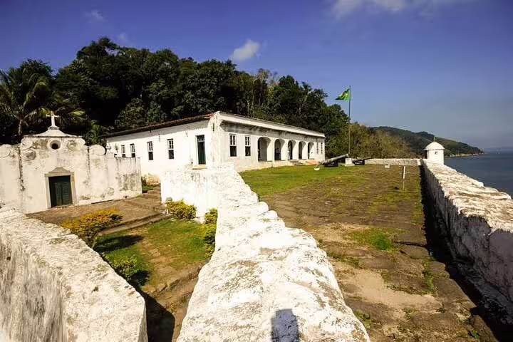 Historic white fort with lush greenery and ocean views, perfect stop on Santos private boat tour with barbecue.