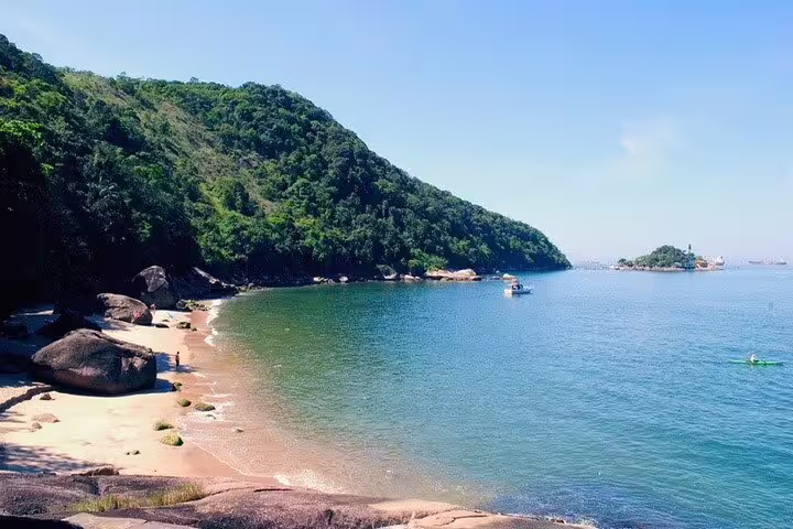 Scenic view of a secluded beach with lush greenery and calm waters, perfect for a serene stop on the Santos boat tour.