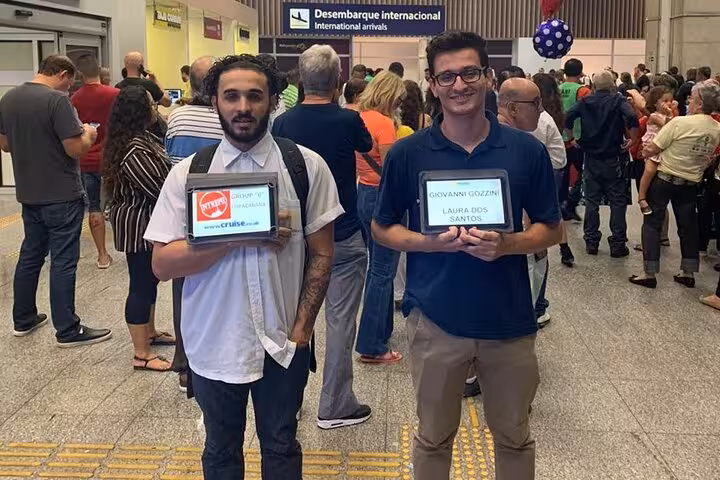 Two people holding name signs at São Paulo airport, ready for shared shuttle service to Paraty.