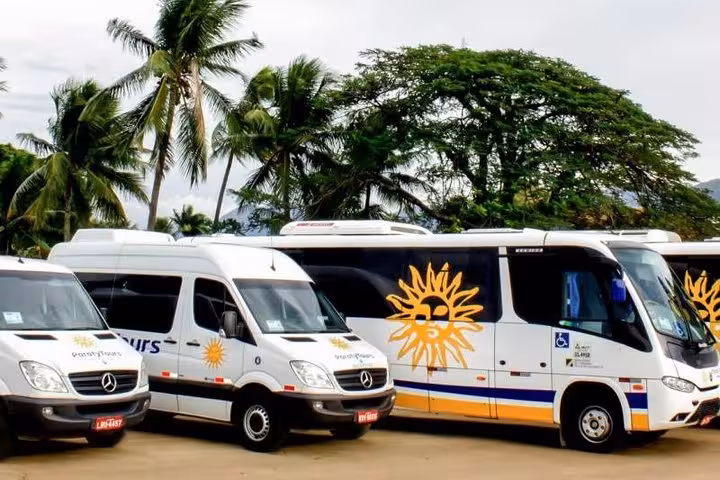 Paraty Tours shuttle buses parked under palm trees, providing transfer from São Paulo to Paraty.