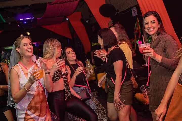 Joyful women enjoying cocktails and dancing in a vibrant São Paulo pub during a lively pub crawl.