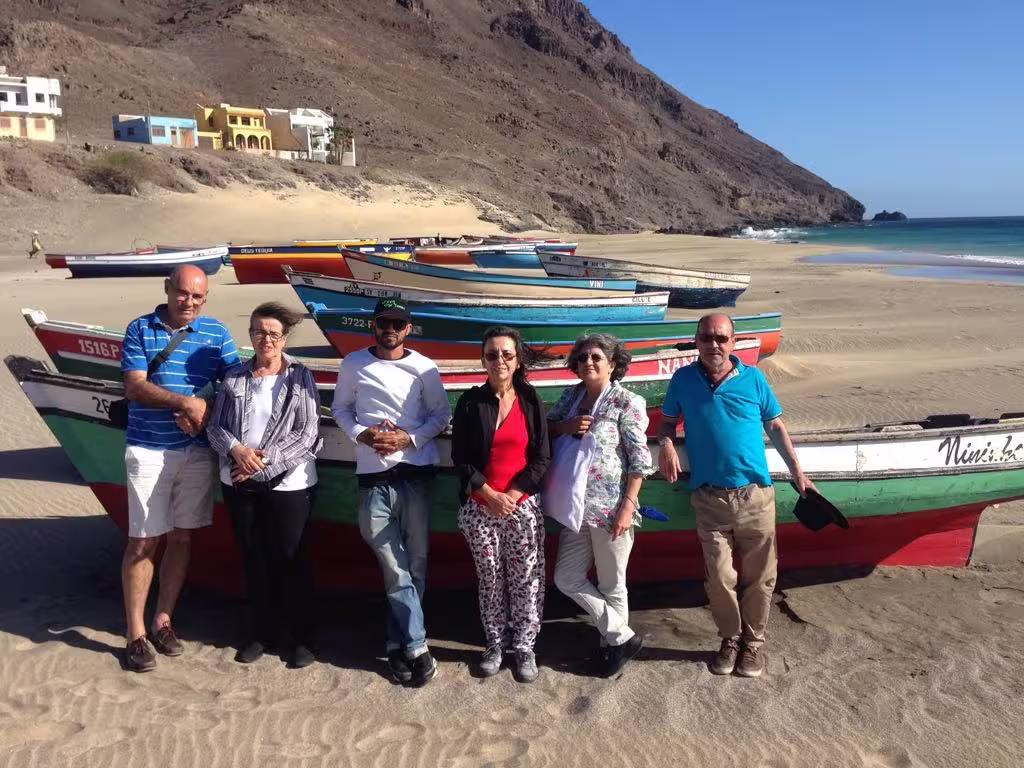 Group of tourists enjoying a sunny day on a picturesque São Vicente beach with colorful fishing boats and scenic views.