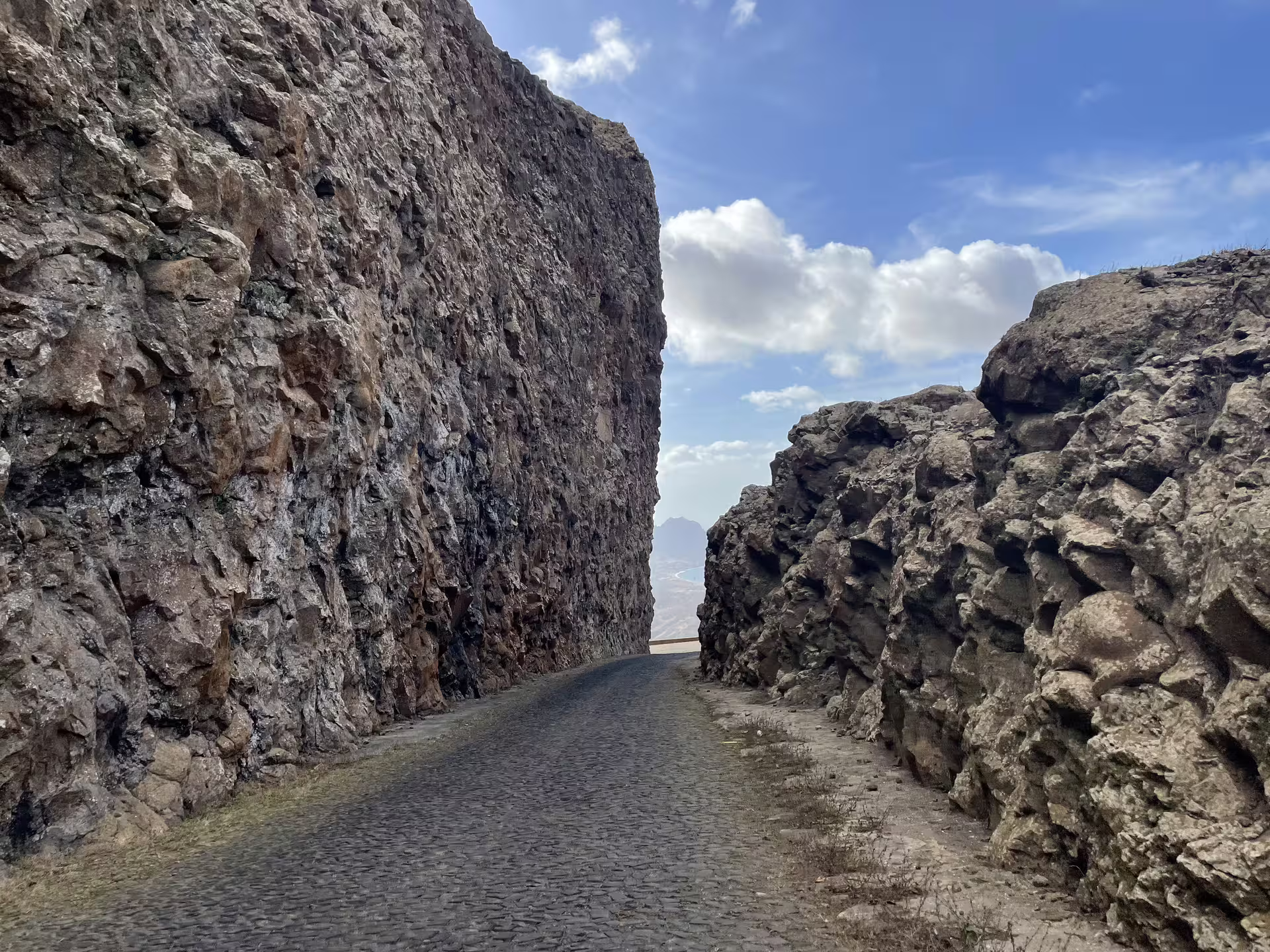 Scenic narrow cobblestone road through towering rock formations on São Vicente island, Cape Verde, under a vibrant sky.