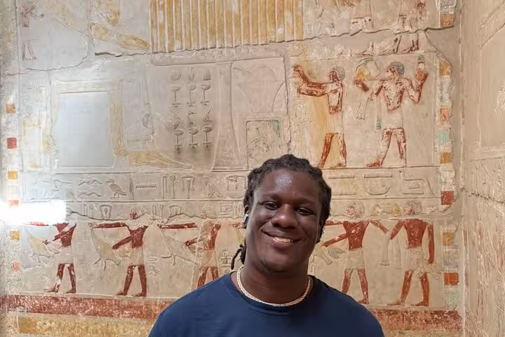 Traveler inside Saqqara tomb with colorful ancient Egyptian wall reliefs on private Giza pyramids tour