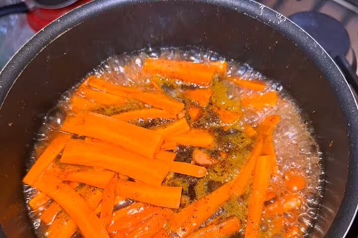 Sliced carrots sizzling in a pan with spices during Sardin Tawa Cooking Class Marrakesh experience.