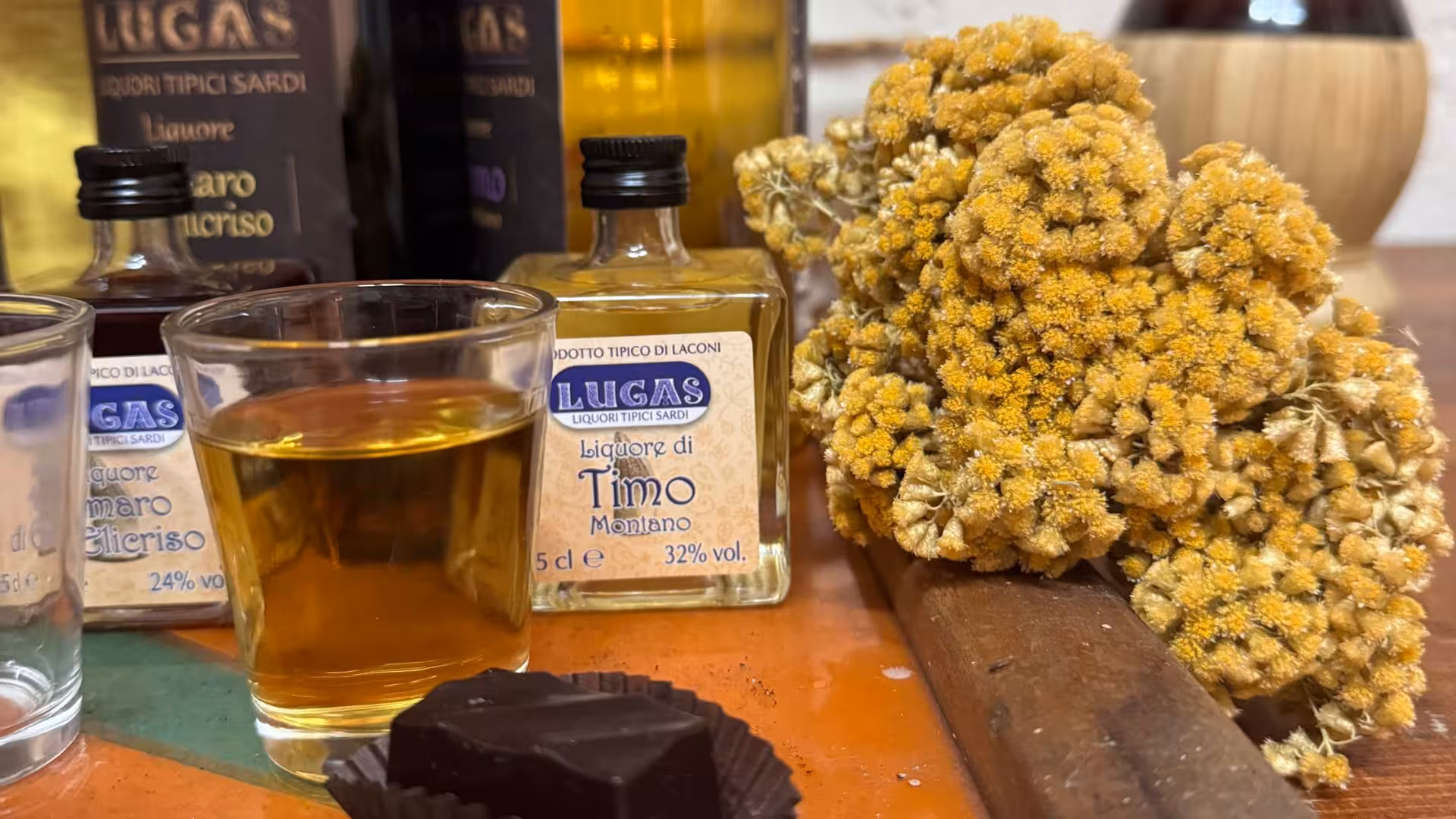 Close-up of Sardinian liqueur with a glass, chocolate, and aromatic herbs, highlighting Laconi's tasting tour.
