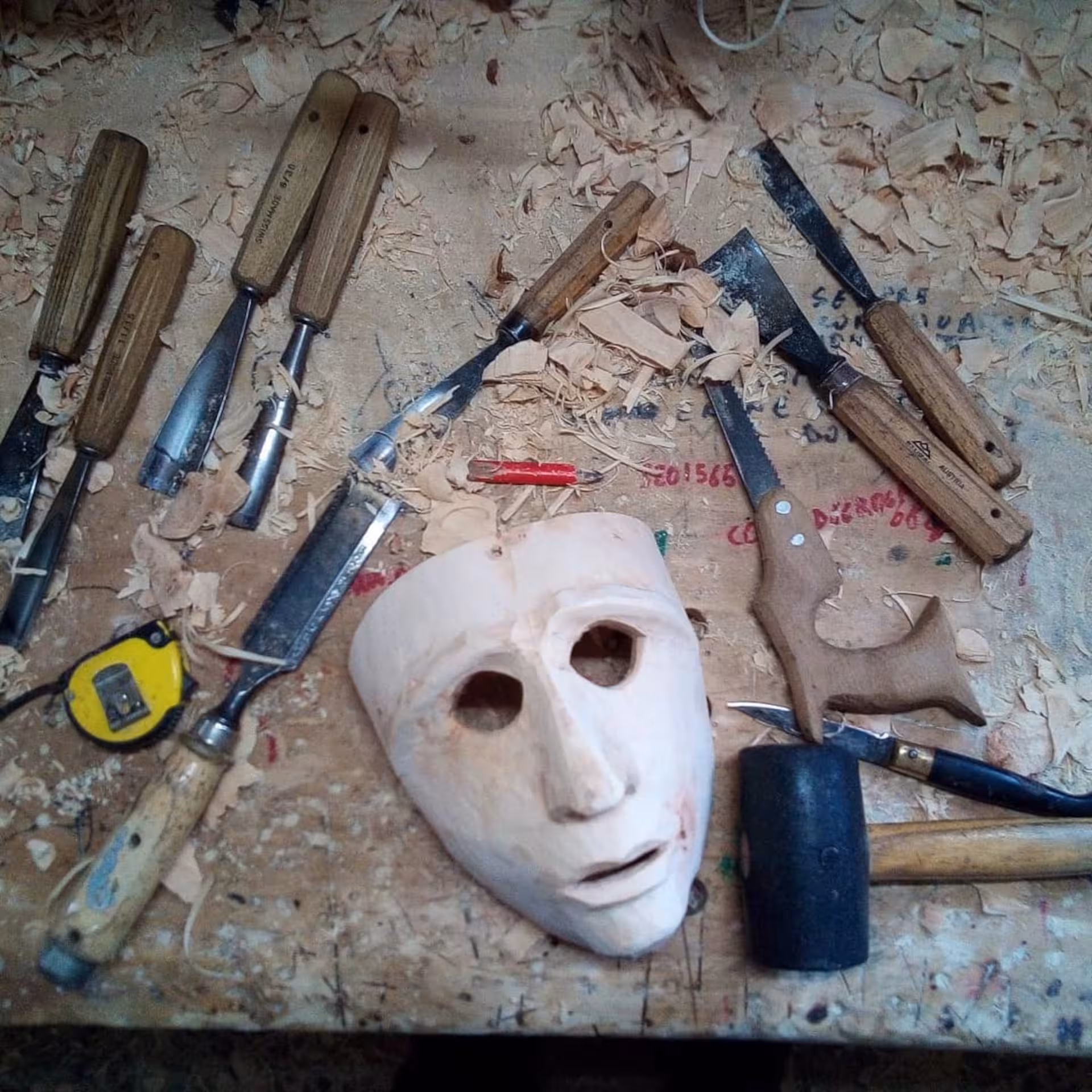Unfinished Sardinian mask surrounded by carving tools and wood shavings in Mamoiada workshop.