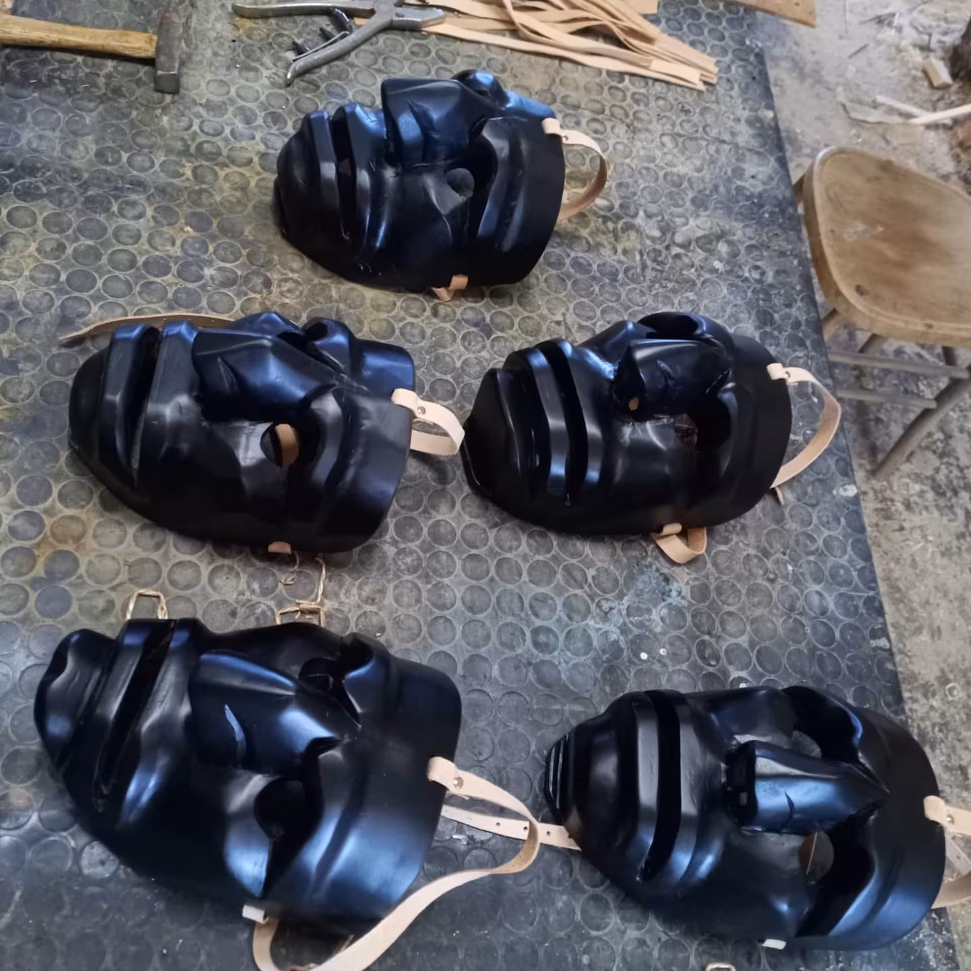 Black Sardinian masks with leather straps displayed on a workshop table in Mamoiada.