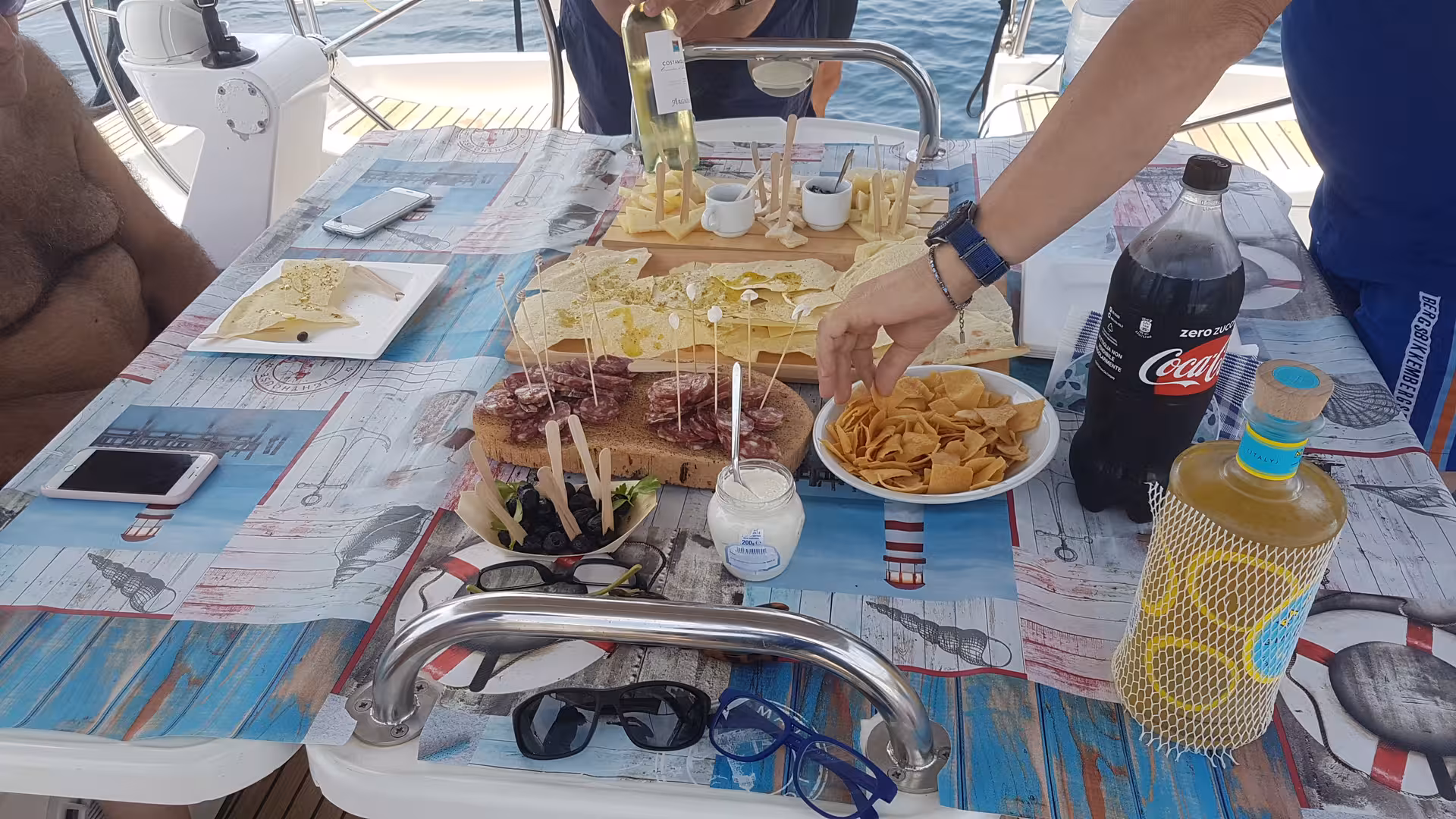 Gourmet spread of Sardinian snacks and drinks on sailboat table during La Maddalena Archipelago excursion.