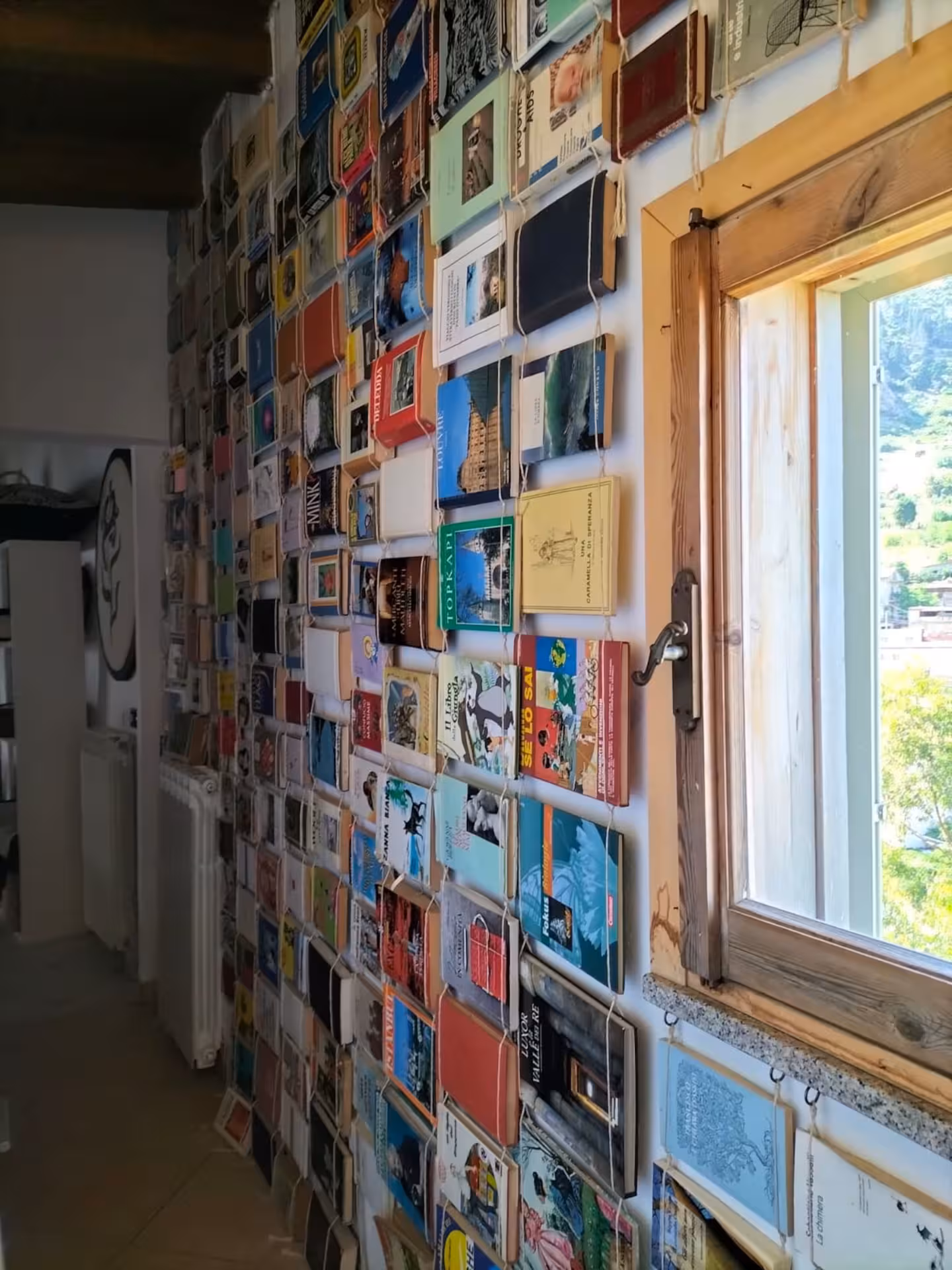 A vibrant wall of colorful books in a Sardinian weaving workshop, showcasing local culture and creativity.
