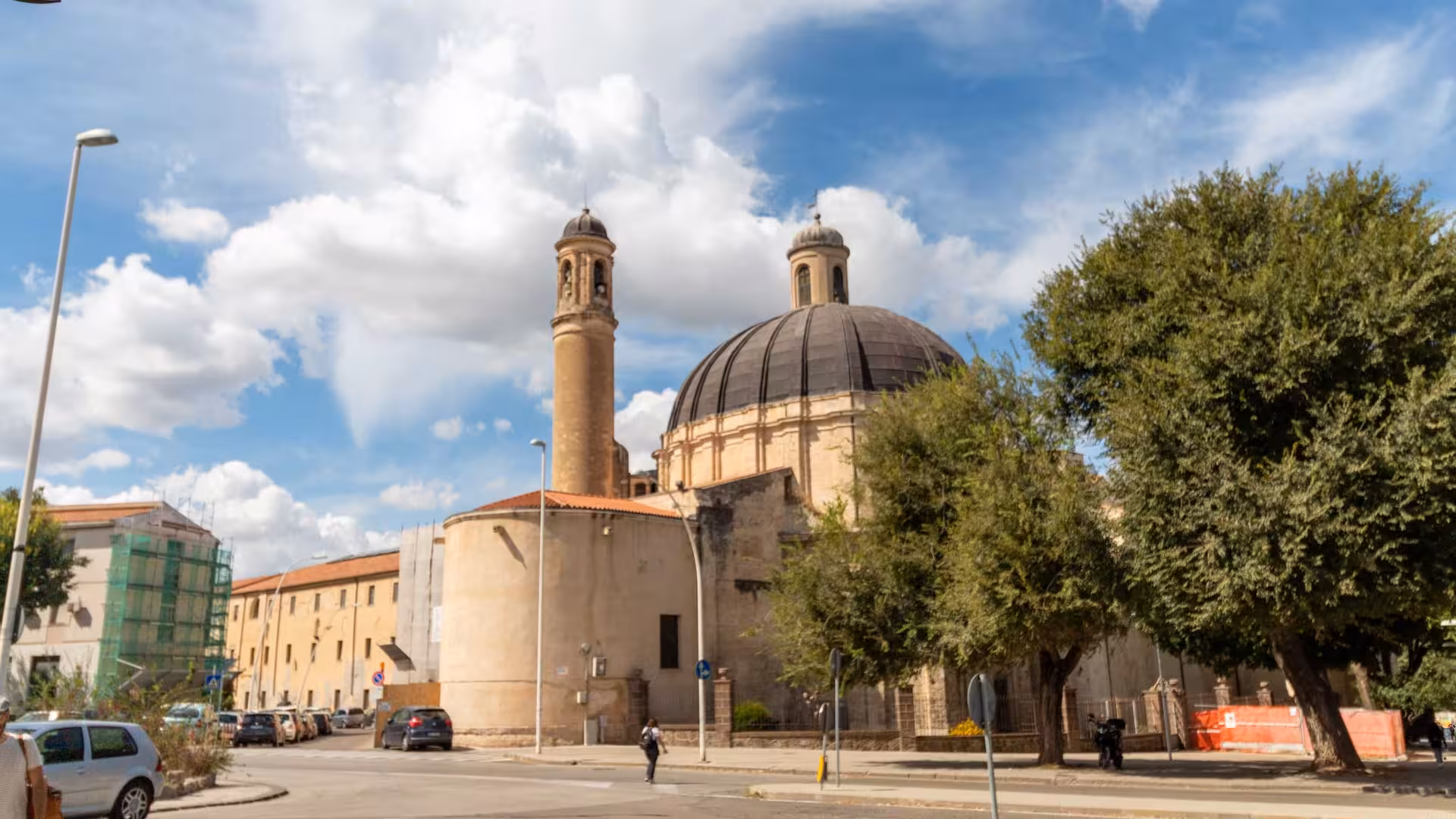 Iconic domed church with towers in Sassari's historic center, framed by lush greenery.