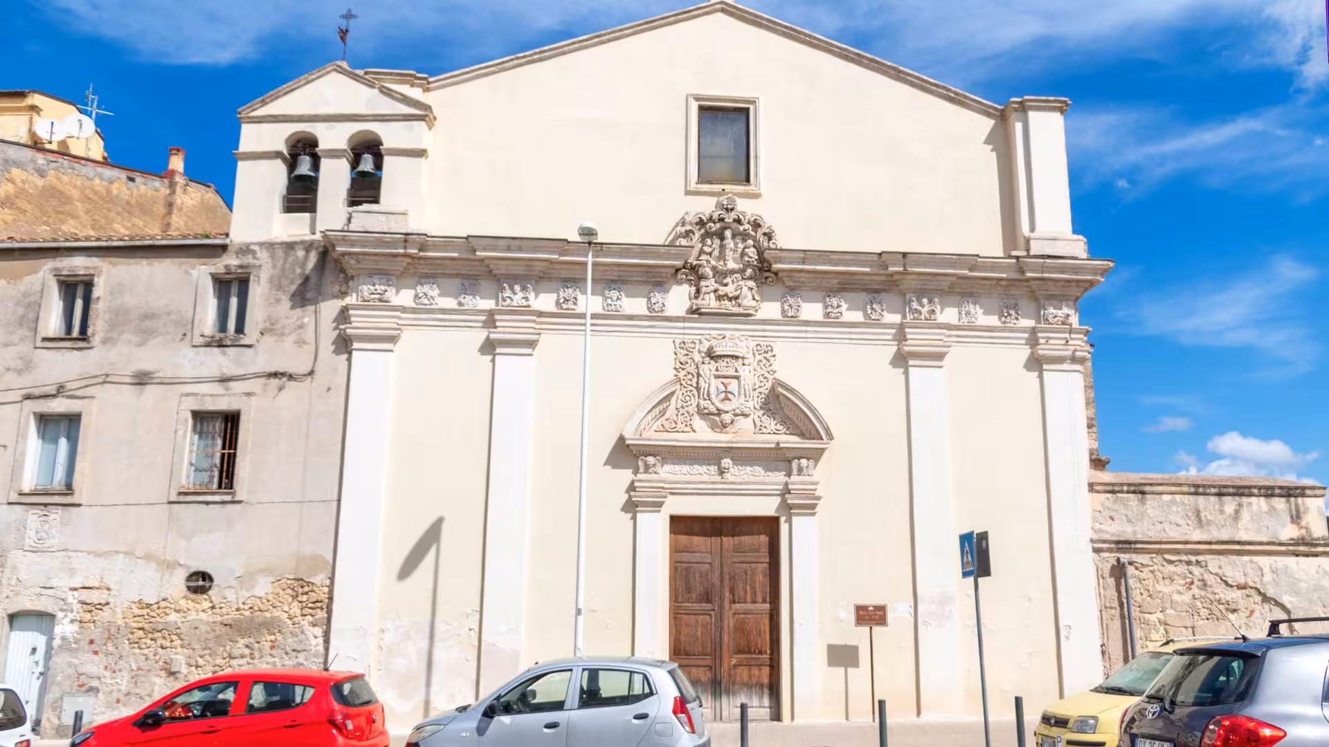 Facade of a historic church in Sassari with detailed carvings and parked cars, ideal for heritage tours.