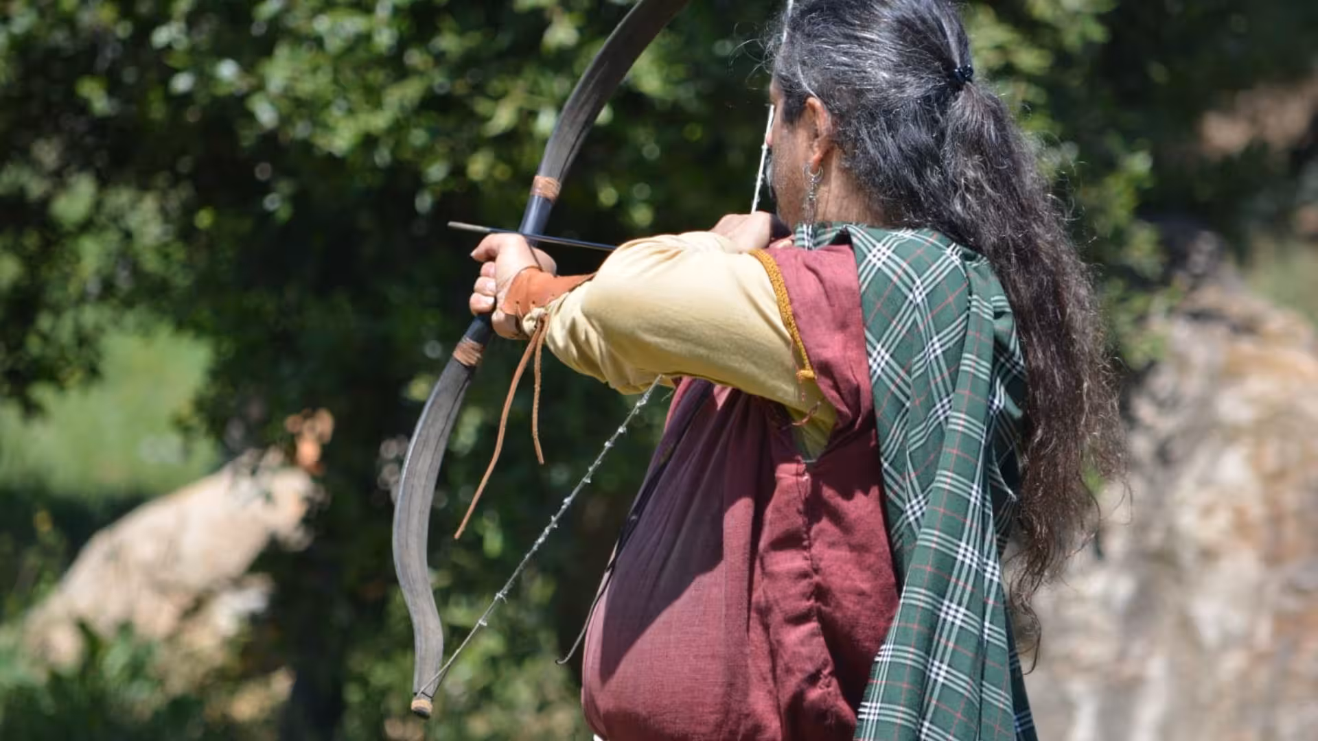 A person in traditional attire practicing archery at Sassari's Roman Castrum educational farm tour.