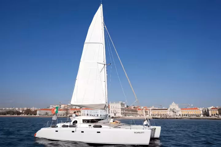 Elegant sailing catamaran 'Scarlett' cruising on Lisbon waters with a 'Clean & Safe' tourism certification badge.