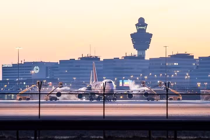 Airplane at Amsterdam Schiphol with control tower at dusk, reliable private departure transfer service