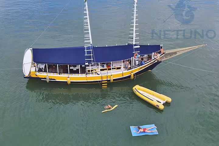 Schooner with blue sails offers paddle and kayak service, as guests relax nearby on a sunny day in tranquil waters.