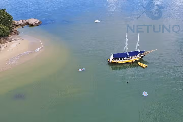 Aerial view of a schooner anchored near a sandy beach with paddle and kayak service included, set in calm green waters.