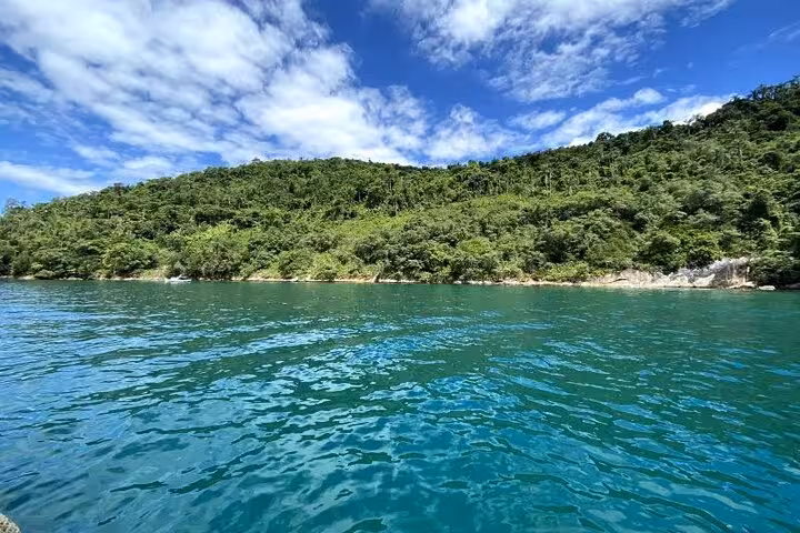 Scenic view of tranquil turquoise waters against a backdrop of lush green hills under a bright blue sky.