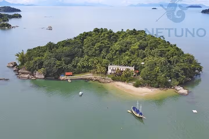 Aerial view of a lush island with a schooner offering standup paddle and kayak services in a tranquil bay setting.