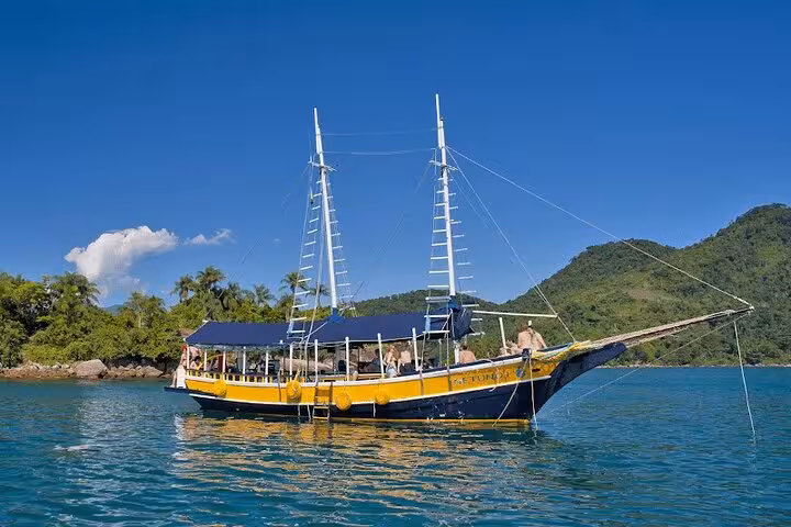 Schooner anchored in tranquil blue waters with onboard standup paddle and kayak service, surrounded by lush hills.