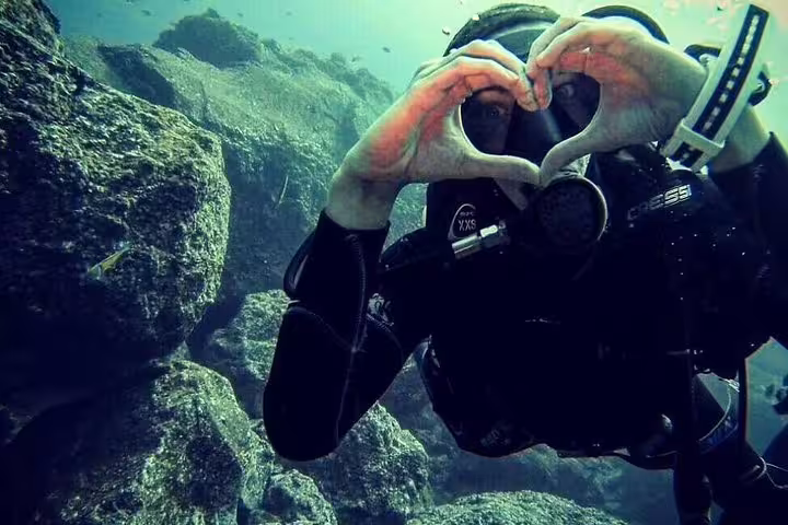 Scuba diver forming a heart shape with hands underwater during an open water course, showcasing marine exploration adventure.