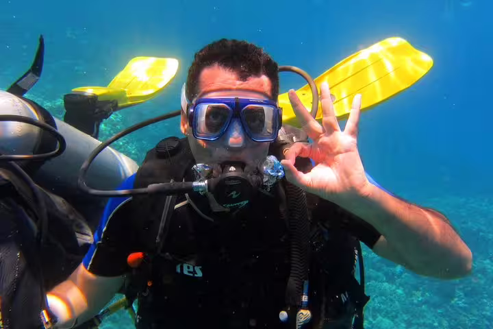 Scuba diver gives OK sign underwater during intro diving and snorkeling day trip, with fins and blue sea