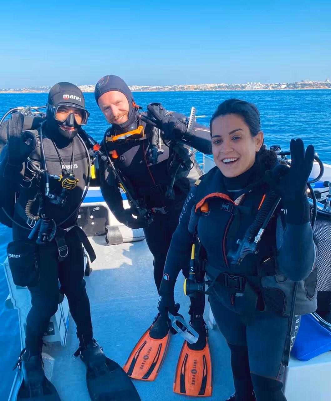 Smiling scuba divers in full gear on Scuba Review boat, ready for guided dive with fins, masks and BCDs