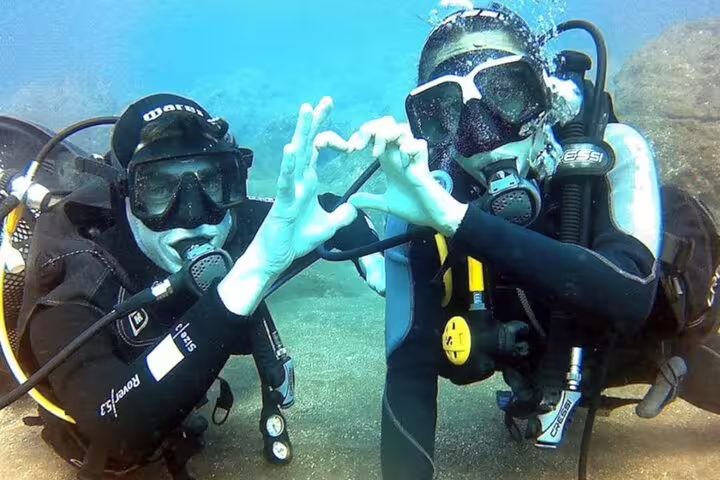 Two scuba divers making a heart shape with their hands underwater during a Try Scuba Diving Experience in Funchal.