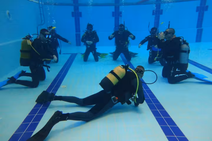 Scuba divers practice skills in a swimming pool during SCUBA REVIEW training, checking buoyancy and gear