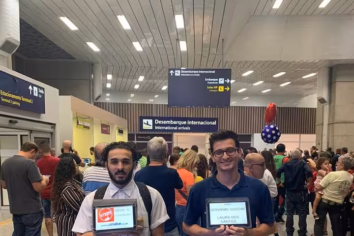 Crowded arrival hall at SDU Airport with greeters holding signs for private transport to Rio de Janeiro hotels.