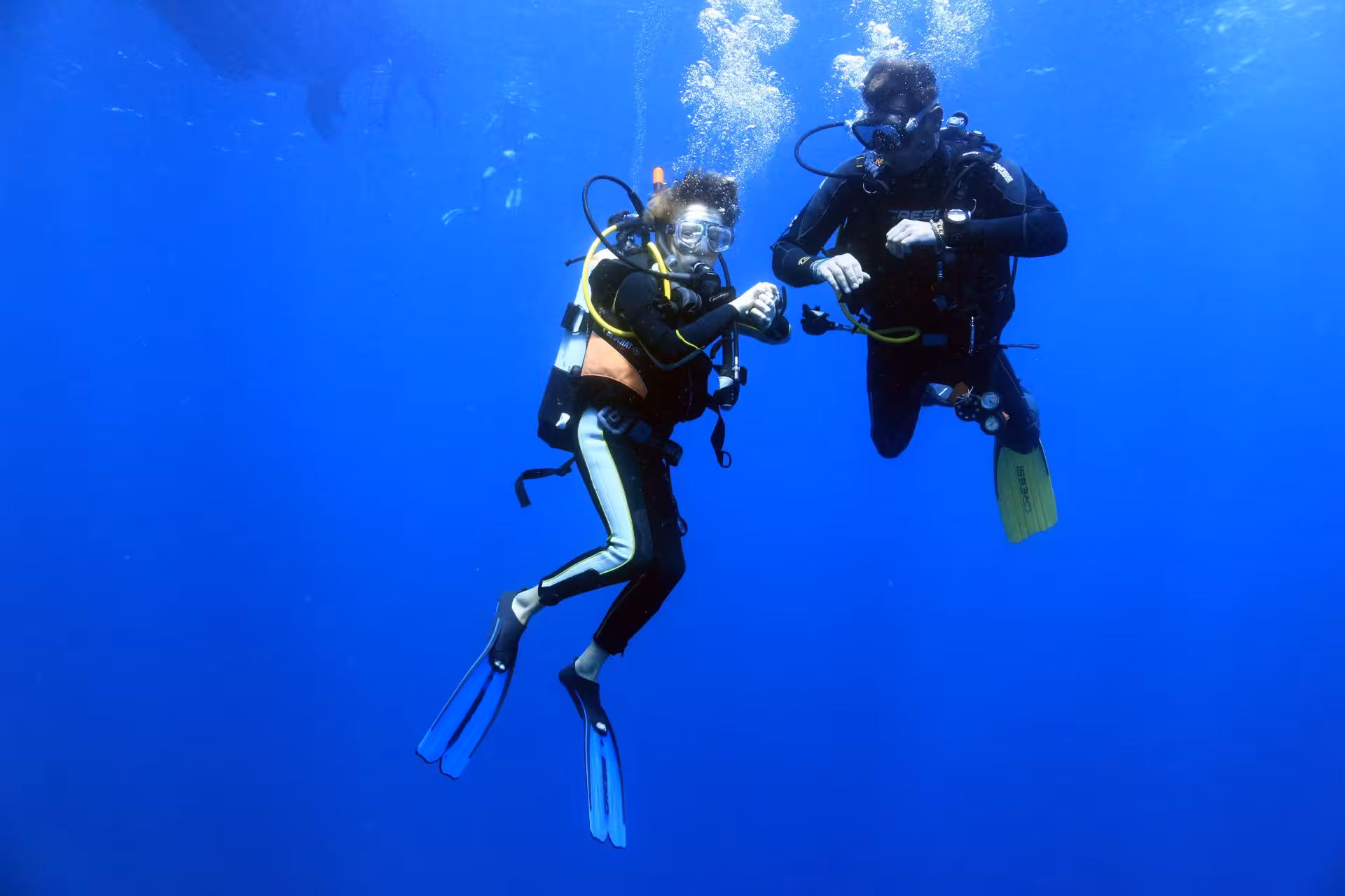 Two divers submerged in clear blue waters at Ruja Island, practicing skills during a sea baptism adventure.