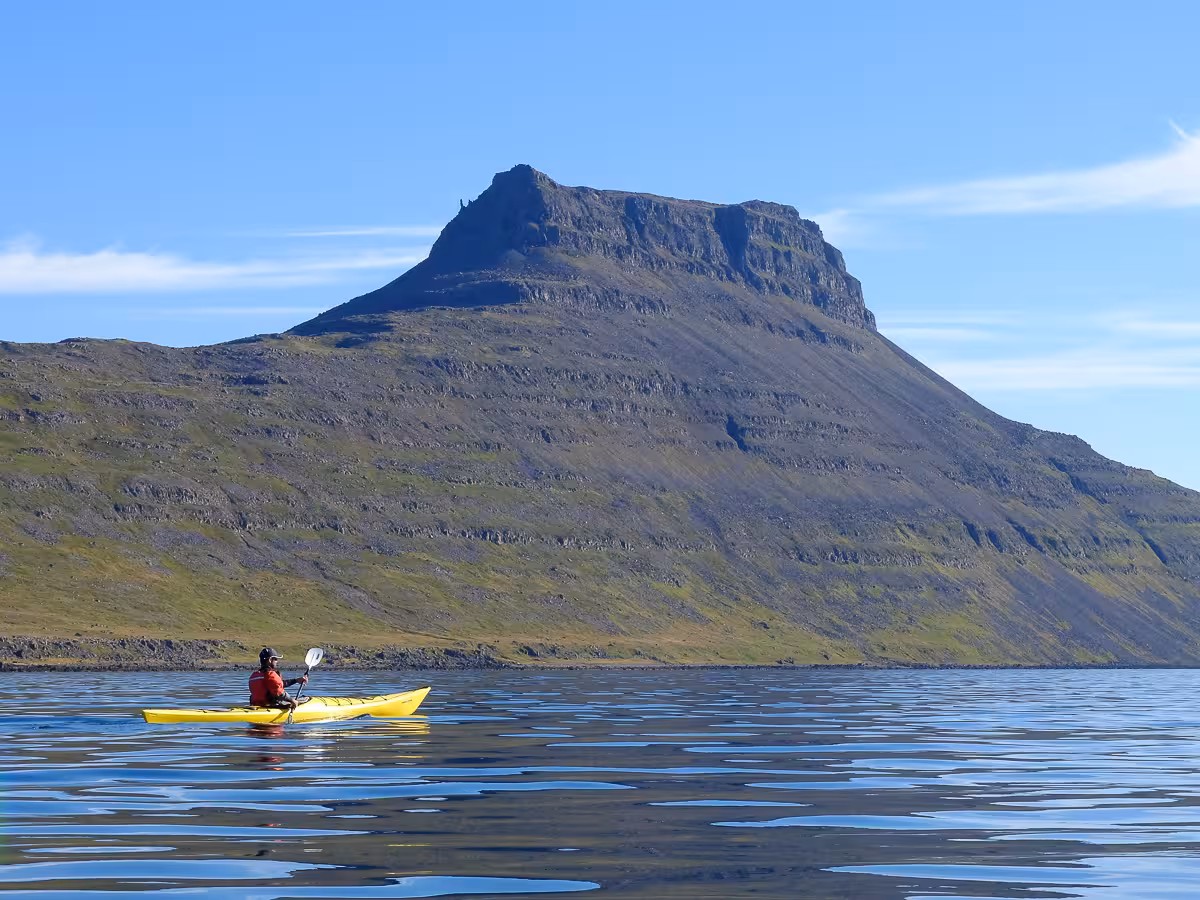 Solo sea kayak on glassy fjord below dramatic peak, part of Solar Eclipse Wild Camp Discovery wilderness tour